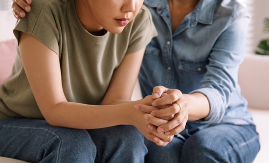 Mother with arm around daughter and holding her hand in comfort