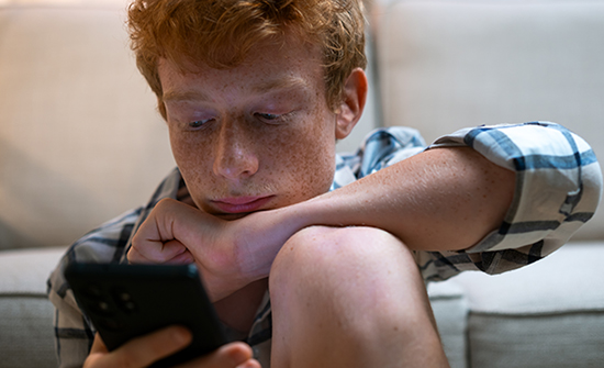 teen boy sitting on floor in front of couch and looking at phone