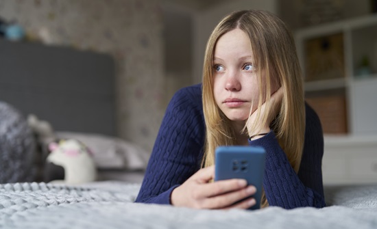 Teen girl lying on her bed, holding her phone and looking away