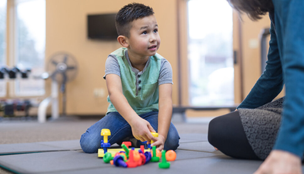 A child plays with toys with an adult watching.