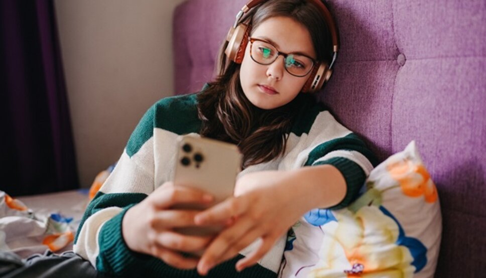 Teen girl sitting and looking at phone with her headphones on