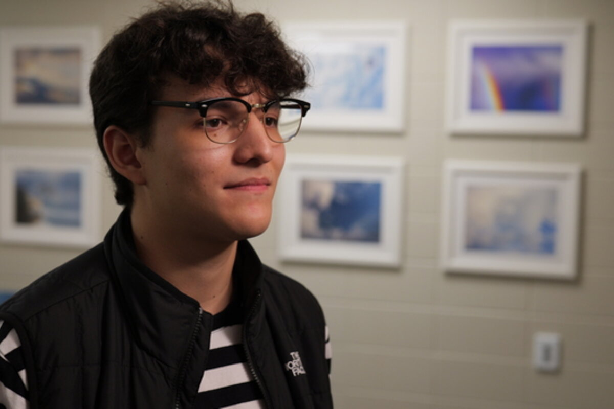 A young man stands in front of a wall of photos.